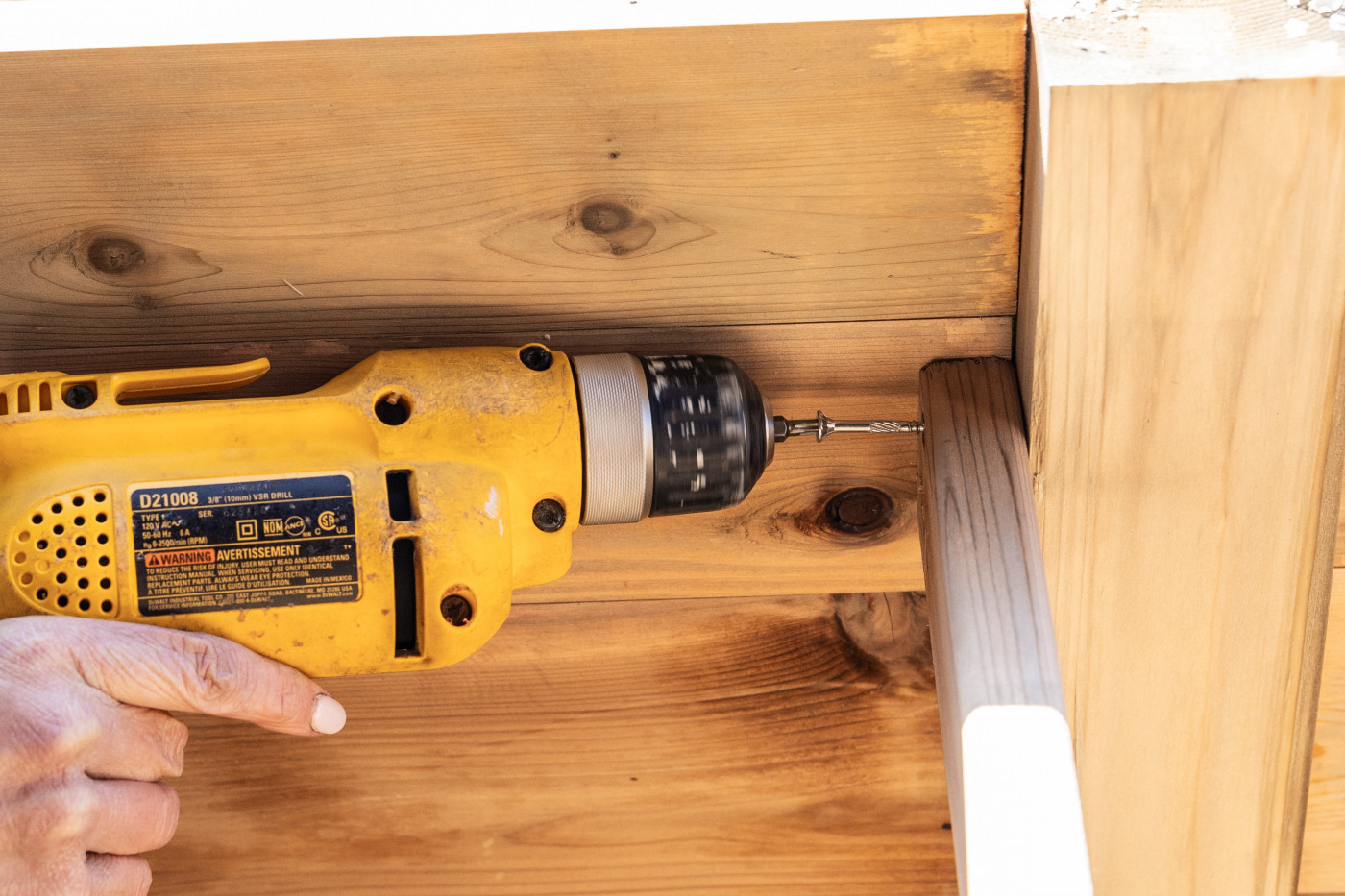 A drill screwing a screw into wood to make a raised bed.