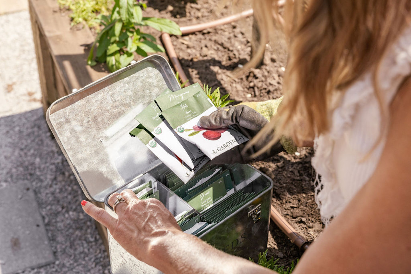person picking seed packets our of seed container in kitchen garden