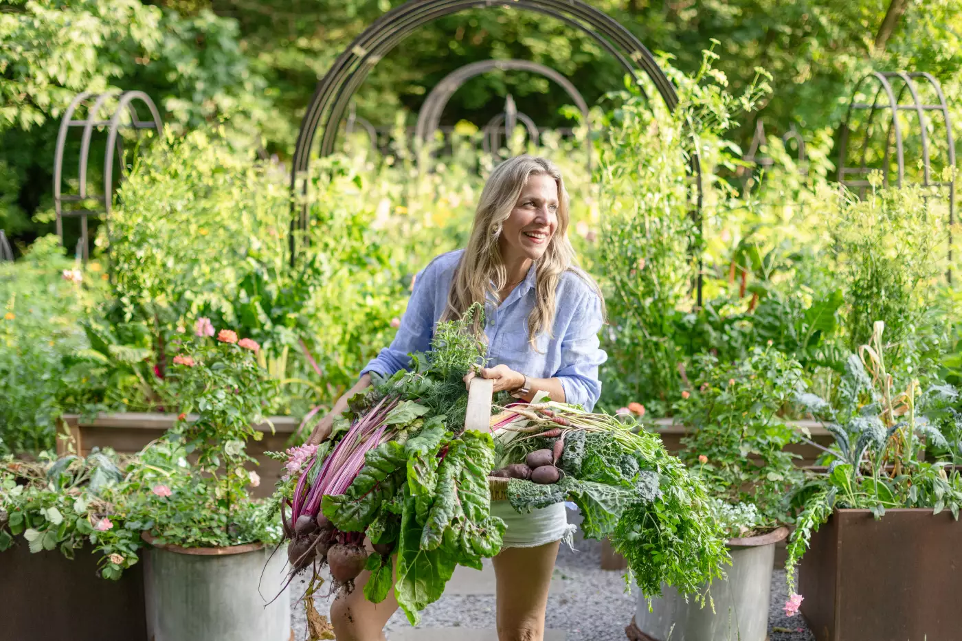 Photo of Nicole Burke in a thriving June garden with lots of plants under an arch trellis